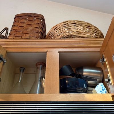 Sale Photo Thumbnail #37: Open wooden kitchen cabinet filled with glassware, a stainless steel Carafe, and ceramic kitchenware, topped with woven storage baskets.