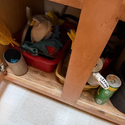 Sale Photo Thumbnail #51: Collection of household cleaning supplies, rubber gloves, spray bottles, and plastic caddies stored under a wooden sink cabinet.