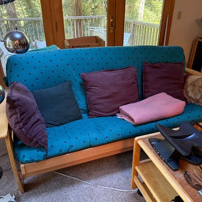 Sale Photo Thumbnail #17: Wooden frame futon sofa featuring a teal patterned cover, accented with various throw pillows and a folded pink blanket.