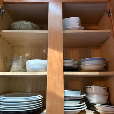 Sale Photo Thumbnail #36: Open wooden kitchen cabinet filled with an assortment of ceramic and glass dinnerware, including stacked plates, cereal bowls, and serving dishes.
