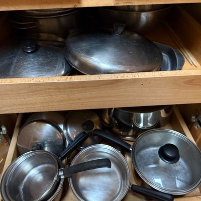 Sale Photo Thumbnail #39: Collection of stainless steel pots, pans, and matching lids stored inside pull-out wooden cabinet drawers.