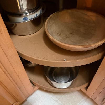Sale Photo Thumbnail #44: Collection of kitchenware stored inside a corner lazy Susan cabinet, including stainless steel mixing bowls, an enamelware bowl, and a large wooden serving bowl.