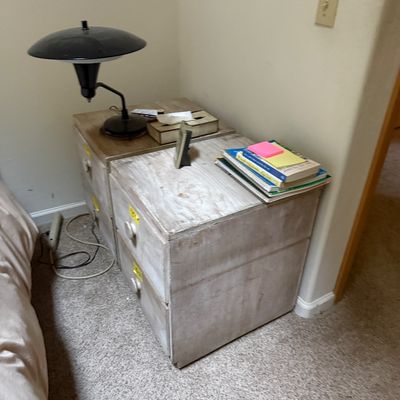 Sale Photo Thumbnail #62: Pair of rustic whitewashed wooden two-drawer nightstands topped with a modern black desk lamp, books, and small accessories.