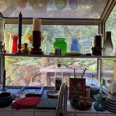 Sale Photo Thumbnail #31: Collection of decorative glassware, vases, candle holders, and knick-knacks arranged inside a garden window sill overlooking trees.