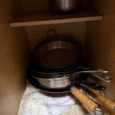 Sale Photo Thumbnail #45: Assorted cookware, including stainless steel pots and pans with metal and wooden handles, stored inside a wooden cabinet.