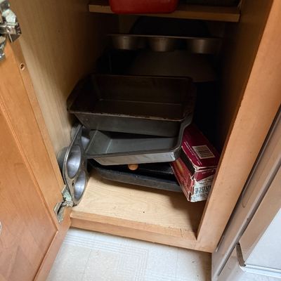 Sale Photo Thumbnail #40: Collection of assorted bakeware, including loaf pans, muffin tins, and colorful enamel baking dishes stored in a wooden cabinet.