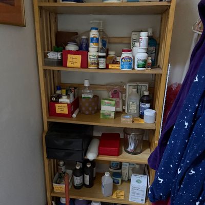 Sale Photo Thumbnail #61: Tall light wood shelving unit stocked with household supplies, over-the-counter medications, paper products, and cleaning goods.