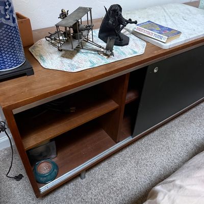 Sale Photo Thumbnail #65: Mid-century modern low wood credenza featuring open shelving and a sliding black door, decorated with a metal biplane model and other collectibles.