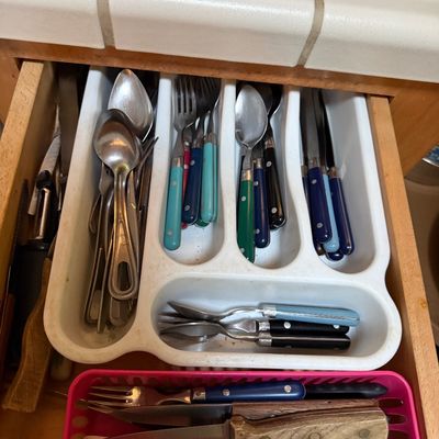 Sale Photo Thumbnail #46: Open kitchen drawer filled with an assortment of flatware, including stainless steel spoons and colorful plastic-handled utensils, arranged in white and pink organizers.