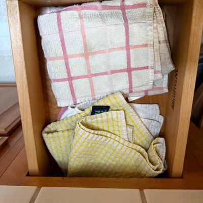 Sale Photo Thumbnail #50: Folded kitchen towels, including plaid and waffle-weave designs, stored inside a wooden cabinet drawer.