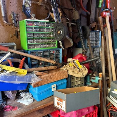 Sale Photo Thumbnail #73: A cluttered workshop workbench featuring small parts storage cabinets, hand tools, long-handled lawn tools, and various storage bins.