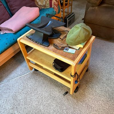 Sale Photo Thumbnail #18: Light wood three-tiered rolling utility cart, holding a black laptop stand, sunglasses, eyeglasses, and an olive green flat cap.
