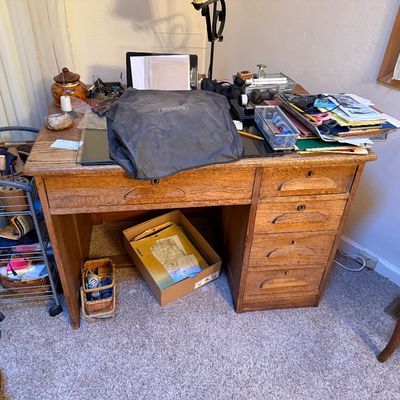 Sale Photo Thumbnail #8: Antique oak pedestal desk with carved drawer handles, topped with various office and crafting supplies, alongside a rolling metal utility cart.