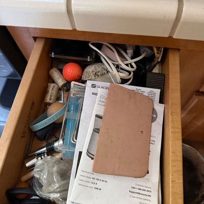 Sale Photo Thumbnail #53: Open wooden kitchen drawer containing assorted household junk items, wine corks, power cords, an orange golf ball, and appliance manuals.