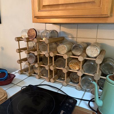 Sale Photo Thumbnail #27: Modular wooden dowel rack filled with glass storage jars containing grains, spices, and dried goods, alongside a black induction cooktop burner and a mint green kettle.