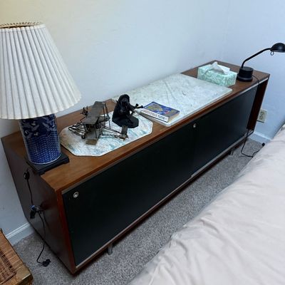 Sale Photo Thumbnail #64: Mid-century modern low credenza with black sliding doors, a marble inset top section, and a blue ceramic table lamp.