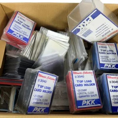 Sale Photo Thumbnail #213: Cardboard storage box filled with assorted trading card protection supplies, including PKK Ultimate Collection top load card holders and rigid plastic cases.