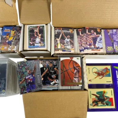 Sale Photo Thumbnail #12: Collection of 1990s NBA trading cards stored in cardboard monster boxes, hard plastic cases, and a sealed 1991-92 SkyBox blister pack, featuring stars like Magic Johnson, Shaquille O'Neal, and Charles Barkley.