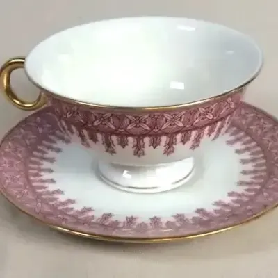 Sale Photo Thumbnail #80: Fine china teacup and saucer set featuring a pink and burgundy geometric border pattern with gold trim and a gilded handle.