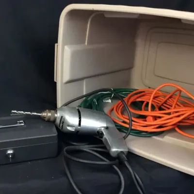 Sale Photo Thumbnail #97: Vintage Craftsman aluminum corded power drill displayed alongside a metal cash box and orange extension cord inside a plastic storage tote.