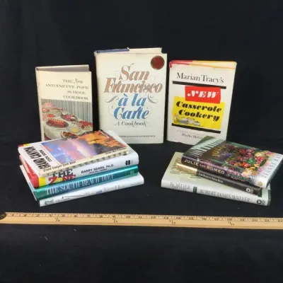 Sale Photo Thumbnail #101: Collection of vintage and modern books, including cookbooks, diet guides, and fiction titles, displayed with a wooden ruler for scale.