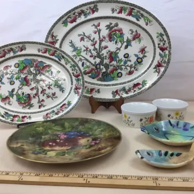 Sale Photo Thumbnail #46: Collection of decorative ceramics featuring two Chinoiserie floral oval platters, a hand-painted fruit design plate, small botanical ramekins, and fish-shaped dishes.