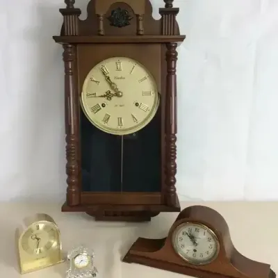 Sale Photo Thumbnail #112: Collection of traditional clocks including a Linden 31-day wooden regulator wall clock, a wooden mantel clock, a brass arched table clock, and a miniature crystal clock.