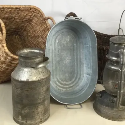 Sale Photo Thumbnail #59: Collection of rustic items including two woven baskets, a vintage metal milk can, an oval galvanized tub, and a vintage metal hurricane lantern.