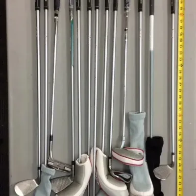 Sale Photo Thumbnail #39: Assorted collection of golf clubs, including drivers, irons, and putters with headcovers, displayed next to a tape measure.