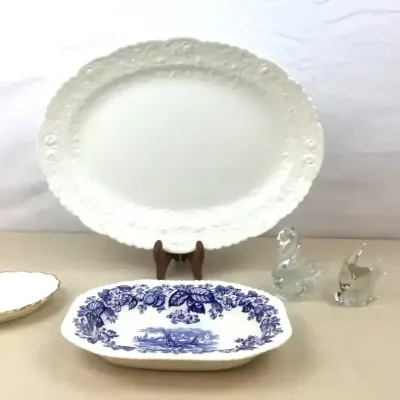 Sale Photo Thumbnail #103: Collection of tabletop decor including a large white ceramic embossed oval platter, a blue and white transferware serving dish, a small gold-rimmed tray, and two clear glass animal figurines.
