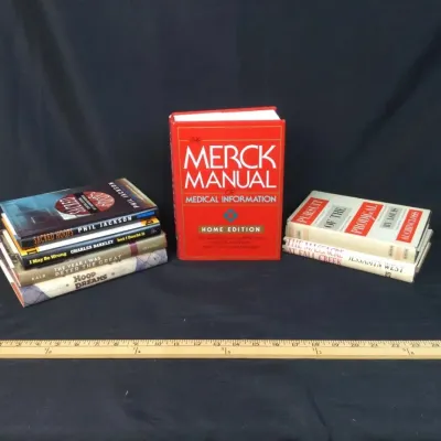 Sale Photo Thumbnail #58: Collection of books including a red hardbound edition of The Merck Manual of Medical Information Home Edition alongside stacks of fiction and non-fiction titles.