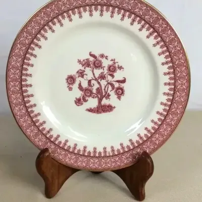 Sale Photo Thumbnail #106: Spode porcelain decorative plate with pink transferware design featuring a central floral tree motif and ornate patterned border with gold trim, displayed on a wooden stand.