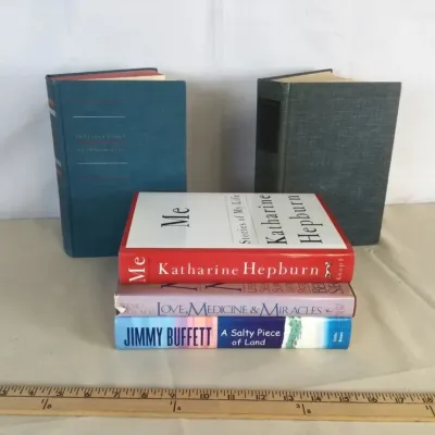 Sale Photo Thumbnail #91: Collection of hardback books including Katharine Hepburn's 'Me', Jimmy Buffett's 'A Salty Piece of Land', and two cloth-bound vintage volumes.