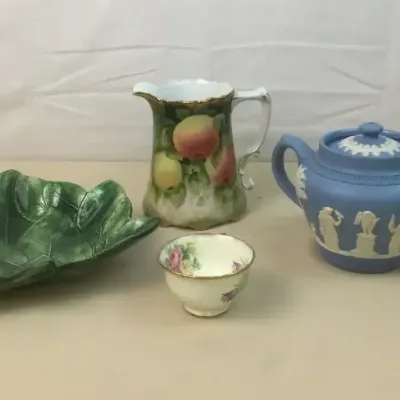 Sale Photo Thumbnail #27: Collection of decorative ceramics, including a blue Wedgwood jasperware teapot, hand-painted fruit porcelain pitcher, green majolica leaf bowl, and small floral teacup.