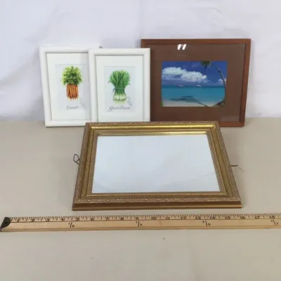 Sale Photo Thumbnail #87: Collection of four framed art pieces and picture frames, including two botanical vegetable prints in white frames, a tropical beach photo in a brown frame, and an ornate gold tone frame.