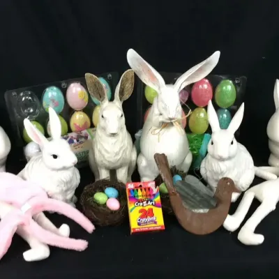 Sale Photo Thumbnail #57: Collection of Easter decorations including white ceramic and resin rabbit figurines, plush bunnies, decorative eggs, and a box of Cra-Z-Art crayons.
