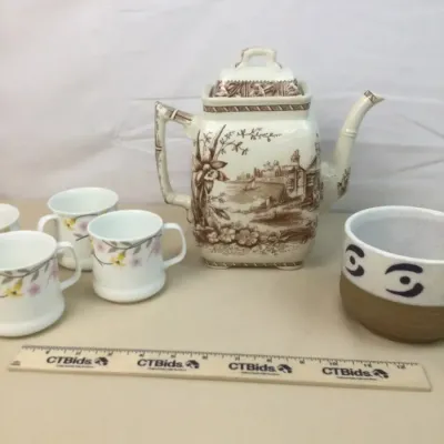 Sale Photo Thumbnail #16: Vintage brown transferware ceramic teapot featuring a scenic landscape design, displayed alongside floral teacups and a stoneware mug.