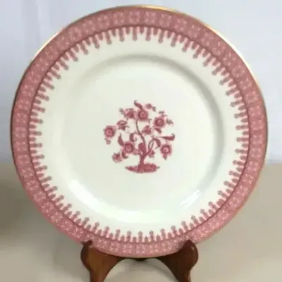 Sale Photo Thumbnail #105: Spode porcelain dinner plate featuring a pink tree floral center motif, ornate border pattern, and gold rim trim, displayed on a wooden stand.