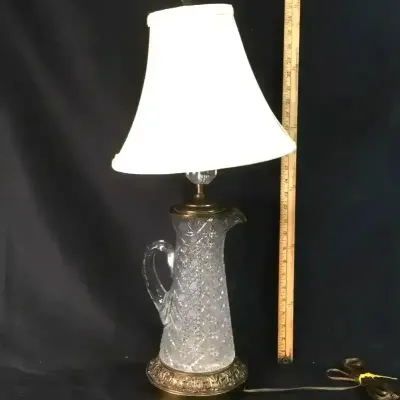 Sale Photo Thumbnail #26: Cut glass pitcher-style table lamp with an ornate brass base and a white fabric bell shade.