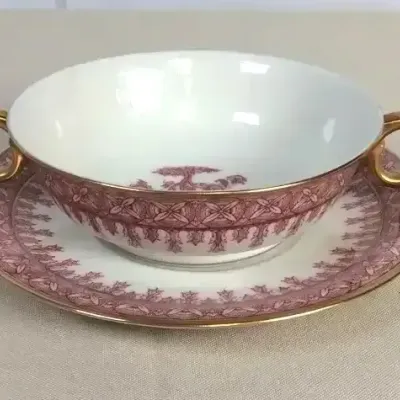 Sale Photo Thumbnail #79: Vintage porcelain double-handled bouillon cup and saucer set featuring a pink transferware pattern with gilt accents.