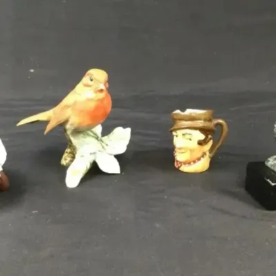 Sale Photo Thumbnail #99: Collection of small vintage figurines, including a lying garden gnome, a painted porcelain bird, a miniature character jug, and a metal bird mounted on a base.
