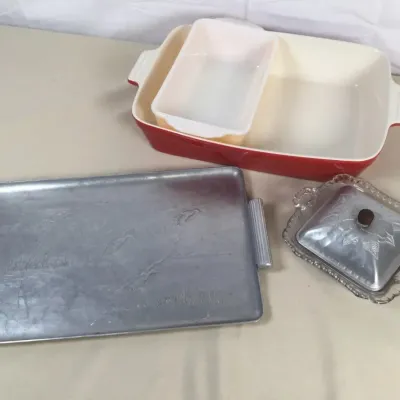 Sale Photo Thumbnail #15: Collection of vintage serveware including a red and white ceramic baking dish with an insert, an etched aluminum tray with side handles, and a pressed glass butter dish with an aluminum lid.