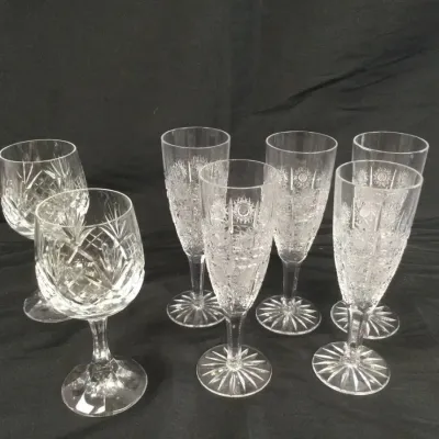Sale Photo Thumbnail #111: Collection of seven cut crystal glassware pieces, including wine glasses and champagne flutes featuring starburst base details and intricate geometric patterns.
