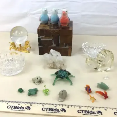 Sale Photo Thumbnail #31: Collection of decorative trinkets and figurines, including glass and stone animals, a clear crystal sphere on a gold-tone unicorn stand, quartz cluster, small glass bowls, and porcelain birds atop a mosaic wood box.