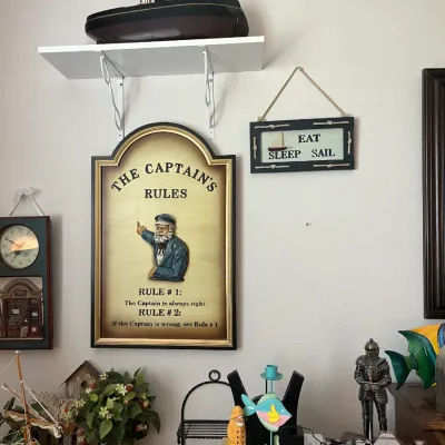 Sale Photo Thumbnail #203: Collection of nautical-themed wall decor and collectibles, including a framed 3D "The Captain's Rules" sign, model ships, and decorative figurines.