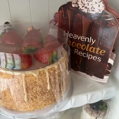Sale Photo Thumbnail #10: Novelty dessert display featuring faux strawberry cake, a chocolate recipe booklet shaped like a cake slice, and mini fake desserts on white shelves.