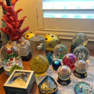 Sale Photo Thumbnail #205: Collection of glass paperweights and snowglobes alongside a coral-motif table lamp and gold star orbs.