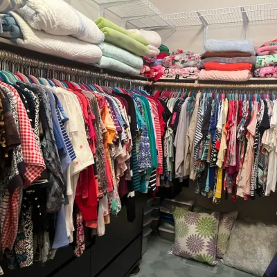 Sale Photo Thumbnail #136: A walk-in closet filled with a large selection of women's clothing, folded blankets, and throw pillows.