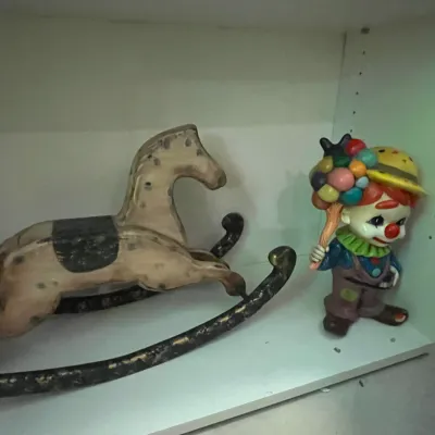 Sale Photo Thumbnail #80: Vintage painted wooden rocking horse figurine displayed on a shelf alongside a colorful ceramic clown figurine.