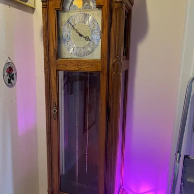 Sale Photo Thumbnail #138: Traditional oak grandfather clock featuring a carved wood case, brass and silver-toned dial, moon dial display, and glass pendulum door.